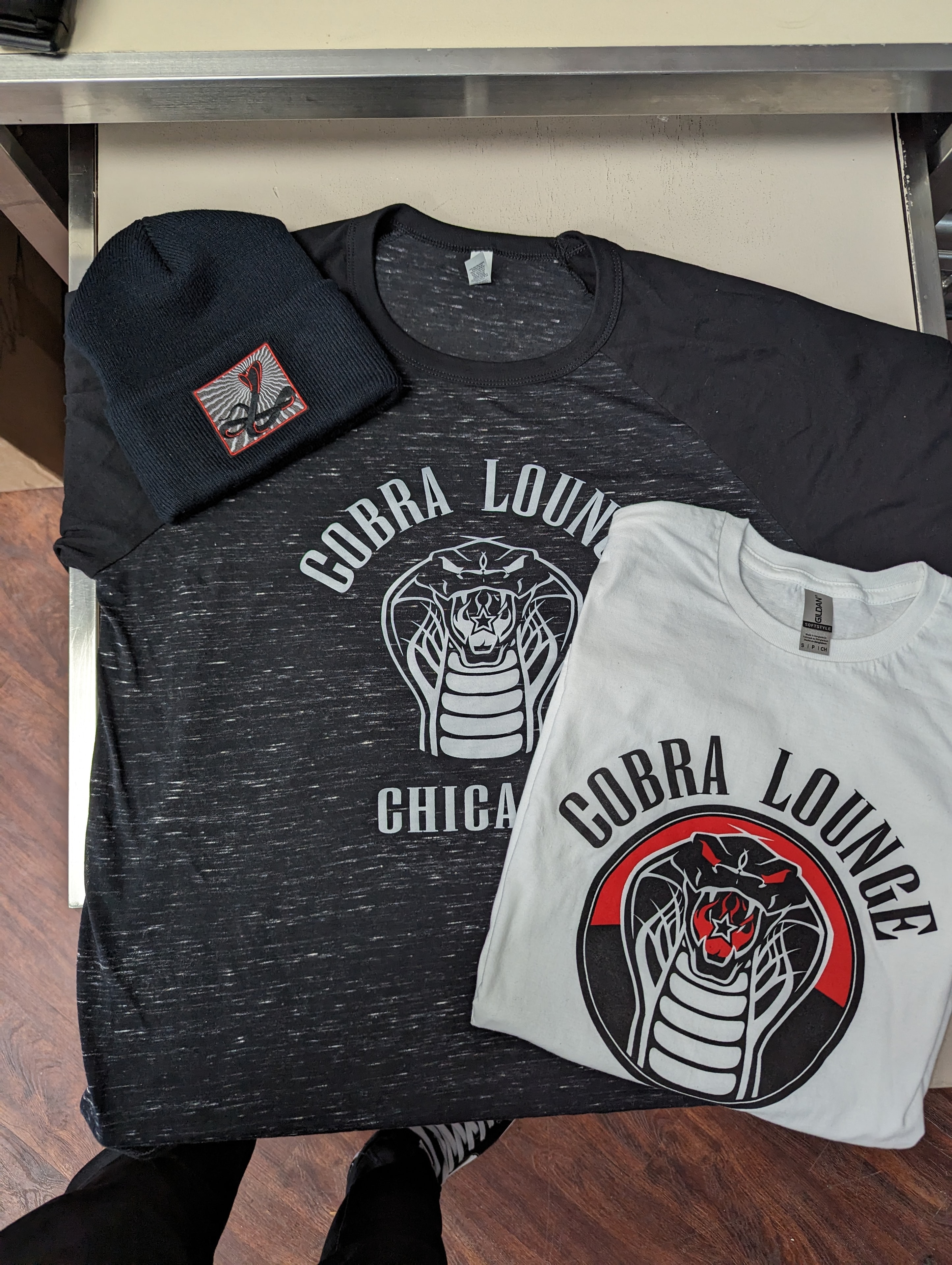 Cobra Lounge merch collection — tees and beanie flatlay